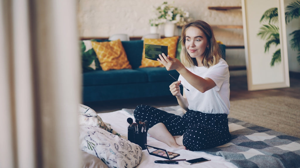 Woman applying makeup while sitting on the floor.