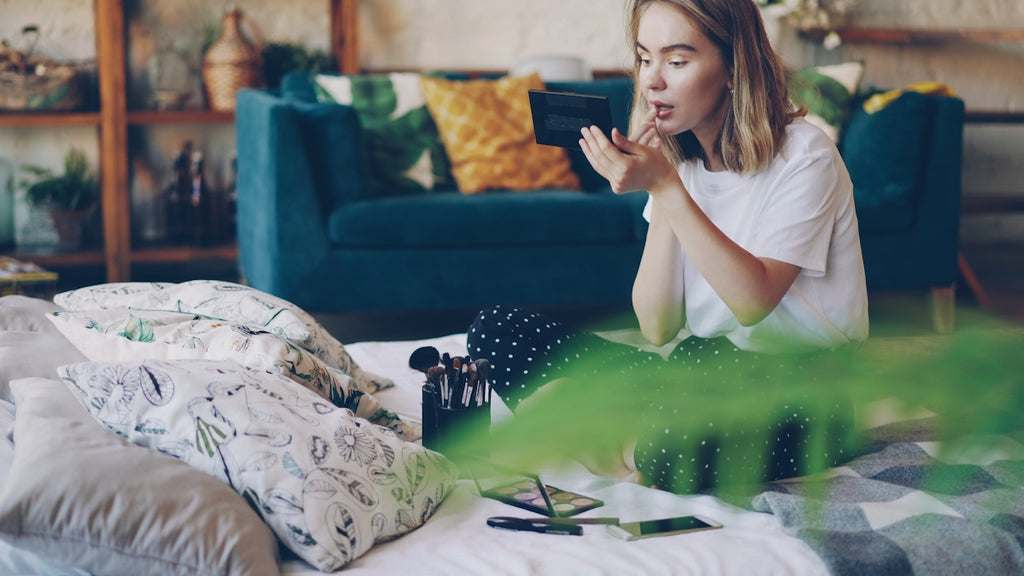 Young woman applying lipstick in bedroom