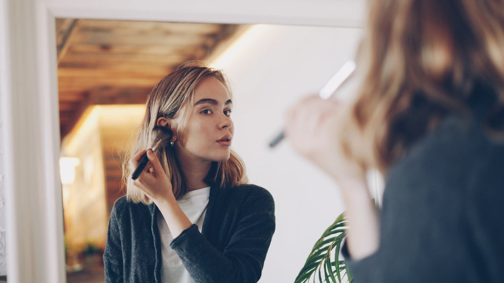 Young woman applying makeup in mirror.