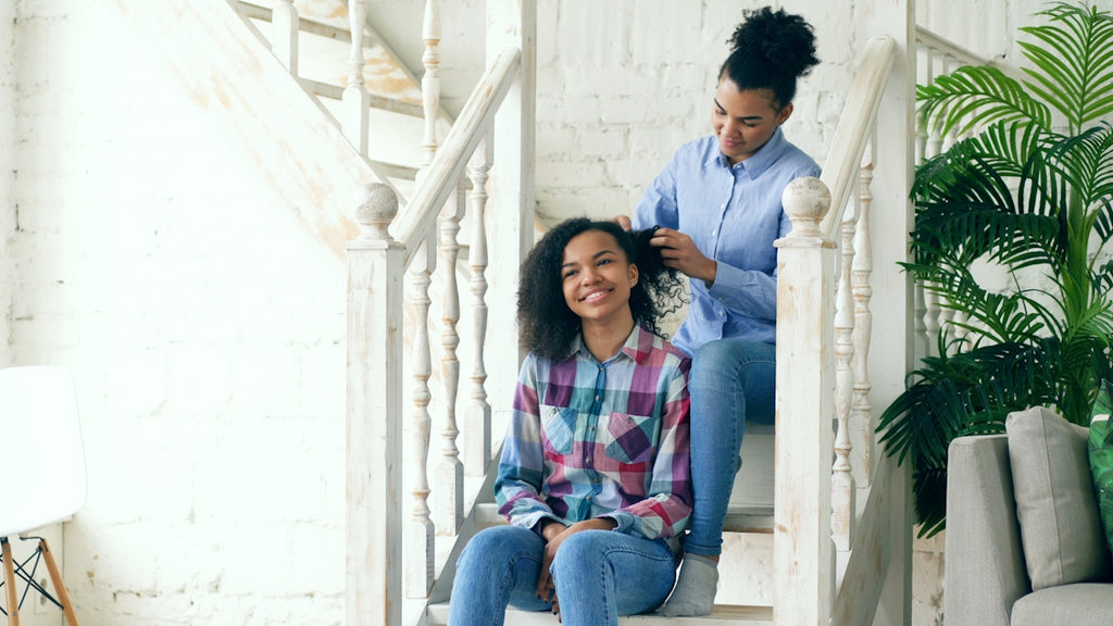 Mother braiding daughter's hair on staircase