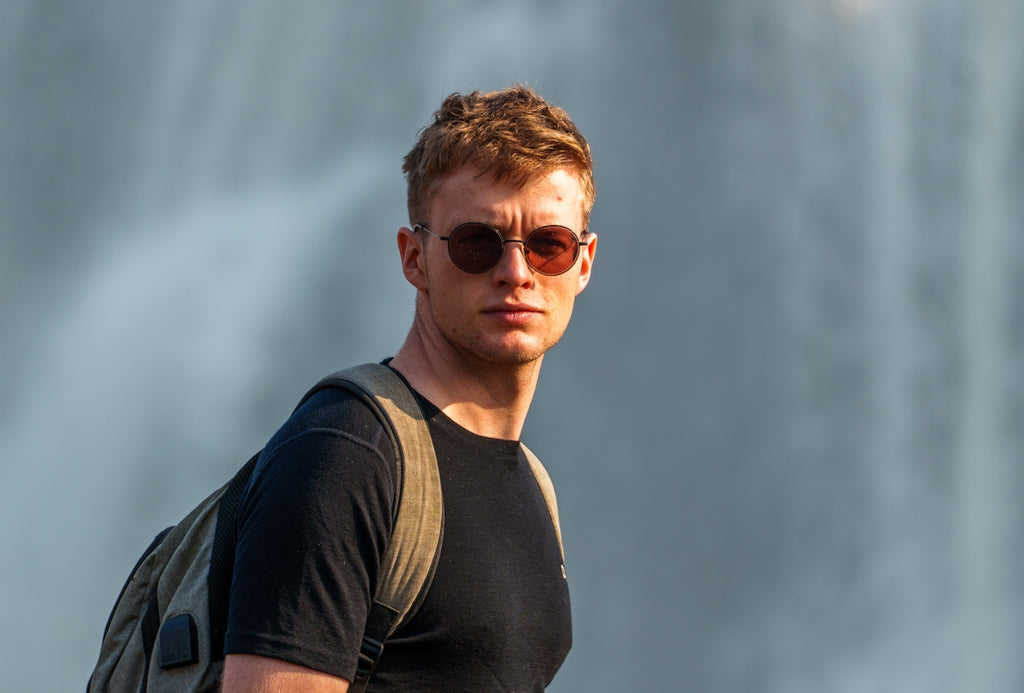 Young man with sunglasses and backpack near waterfall