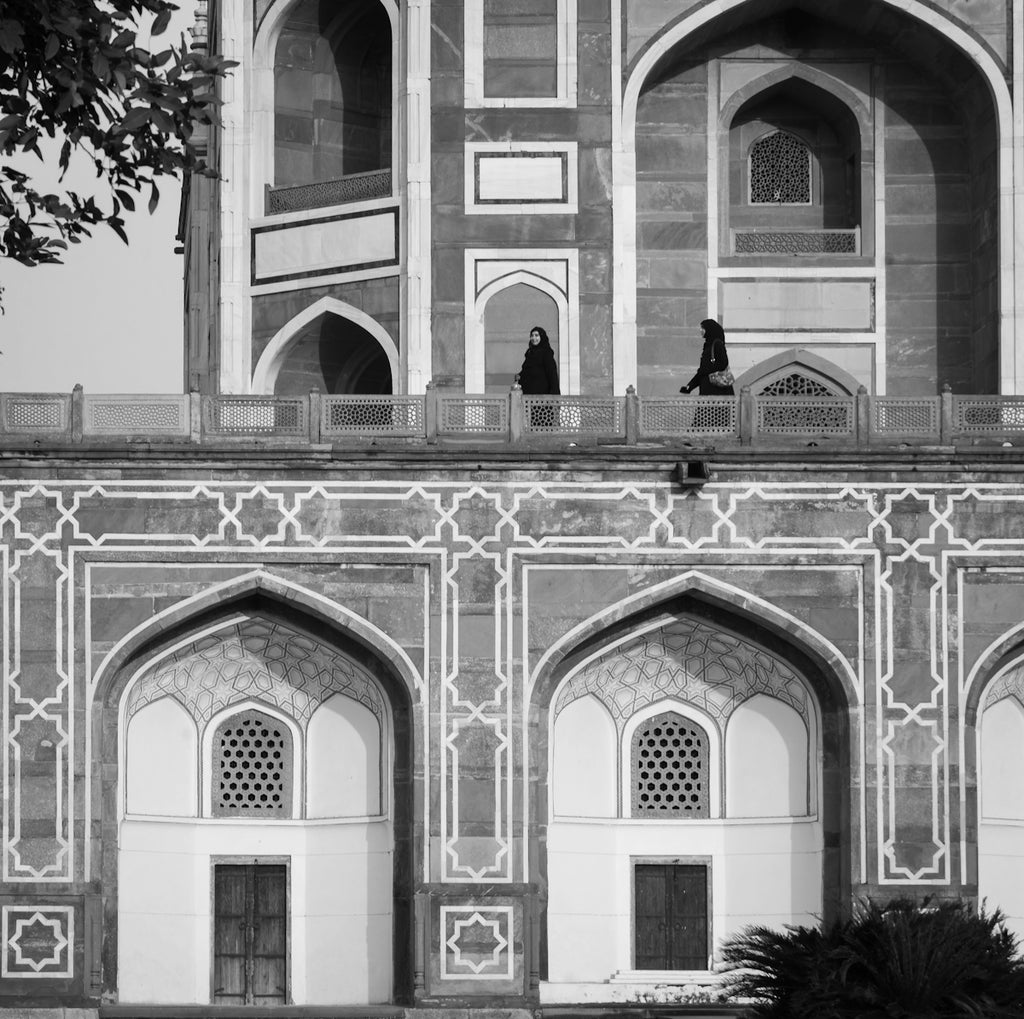 Two women stand on a balcony of an ornate building