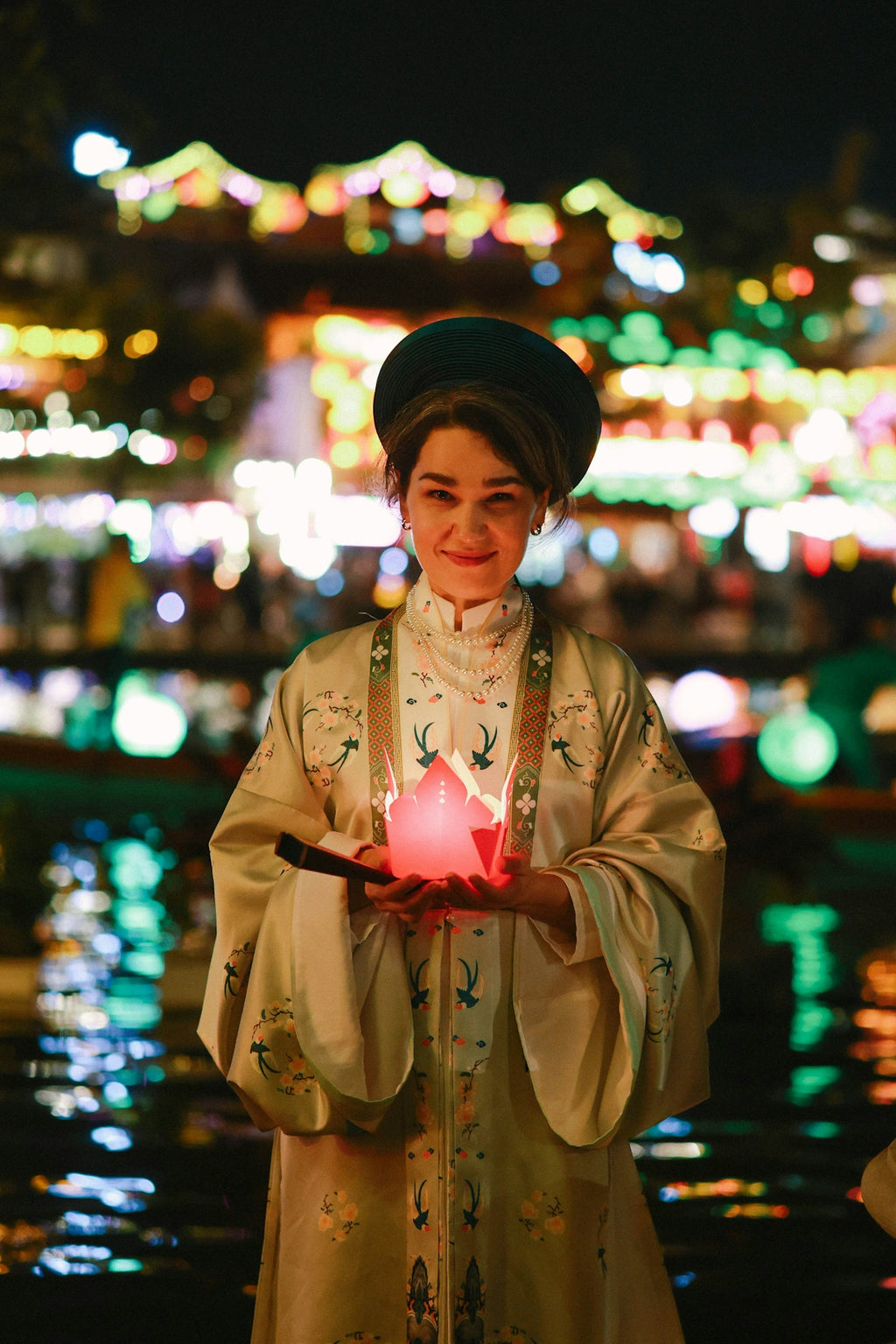 Woman in traditional dress holding a glowing lantern at night.