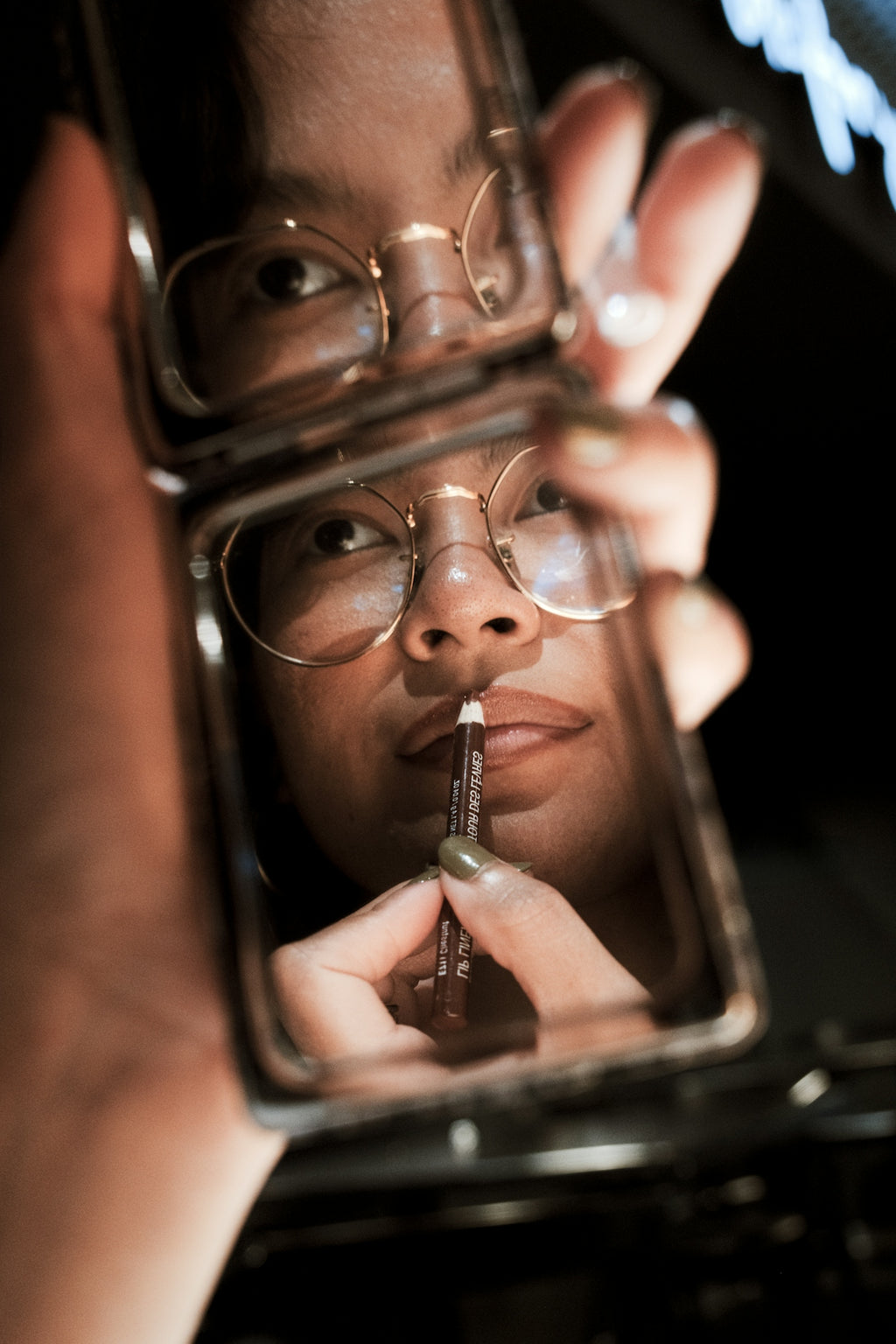 Woman applies lip liner while looking in a compact mirror
