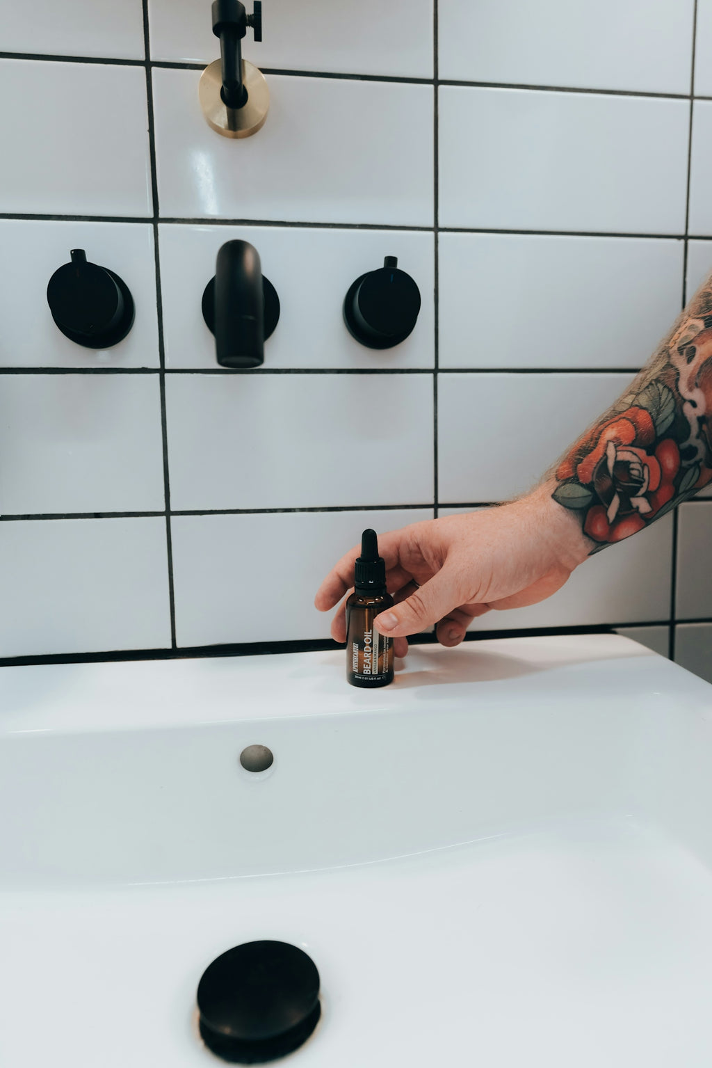 Hand with tattoo reaches for a small bottle.